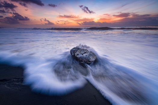 A stunning long exposure of ocean waves crashing over a rock at sunrise, capturing the beauty of nature.