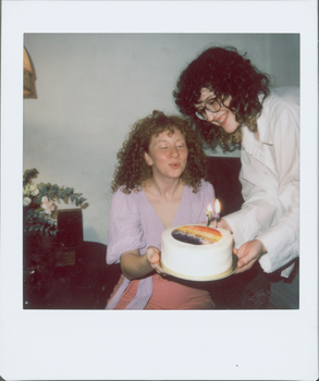 Two women celebrating a birthday with a cake, joyful expressions captured in a candid moment.