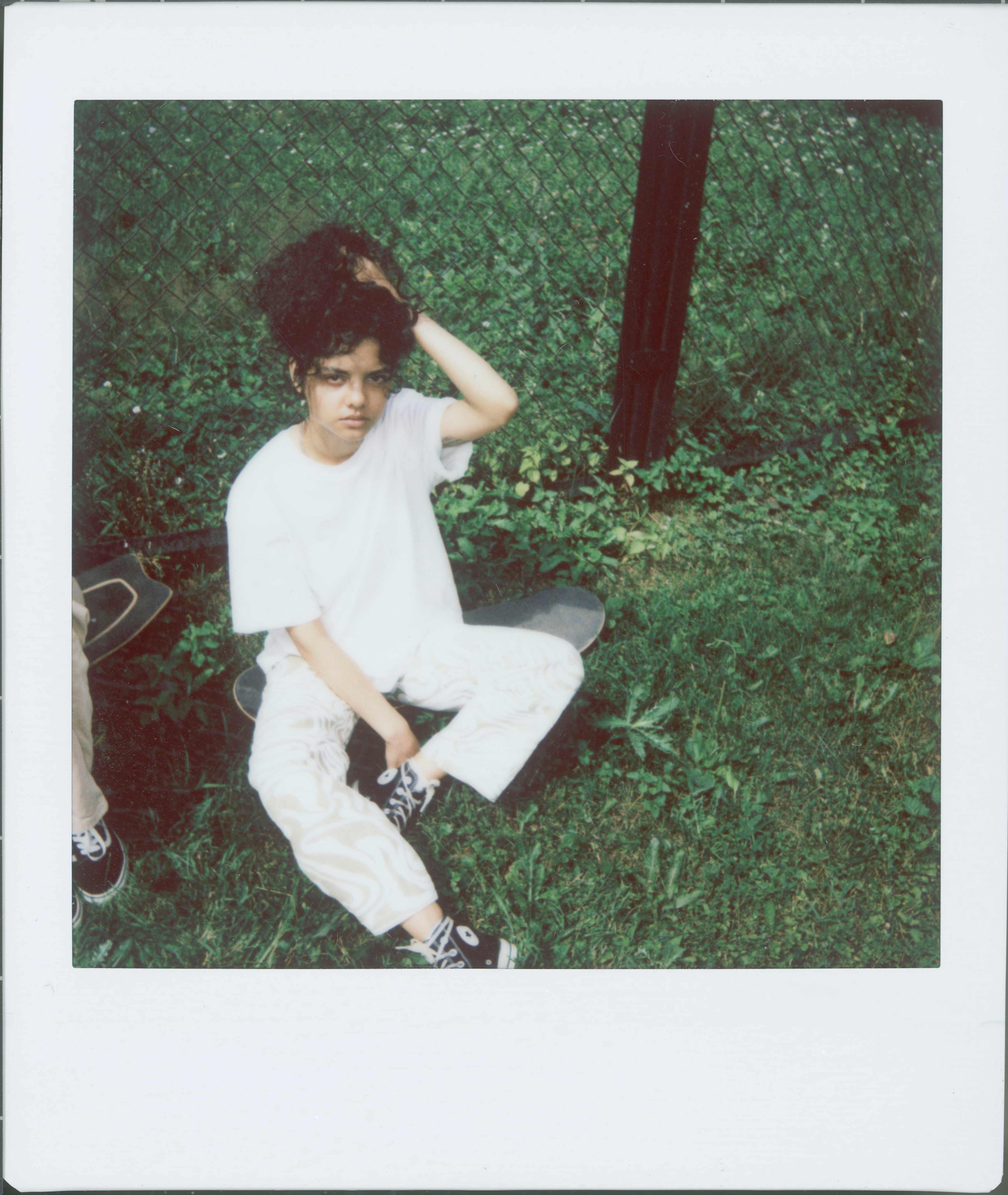 A young woman sitting on grass by a fence, with a relaxed and casual pose.
