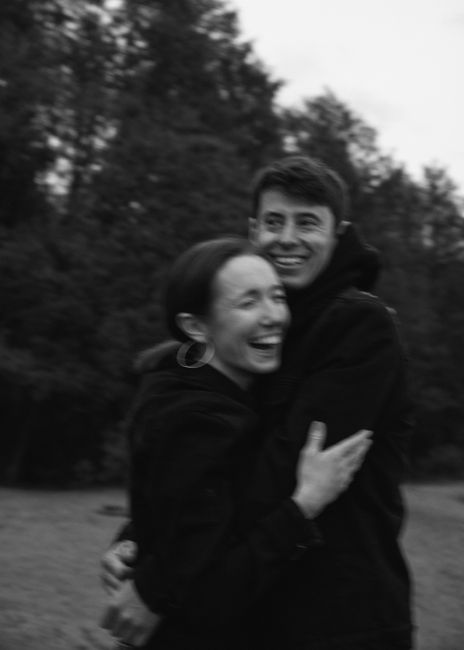 A joyful couple hugging and laughing in a blurred, black and white park scene.