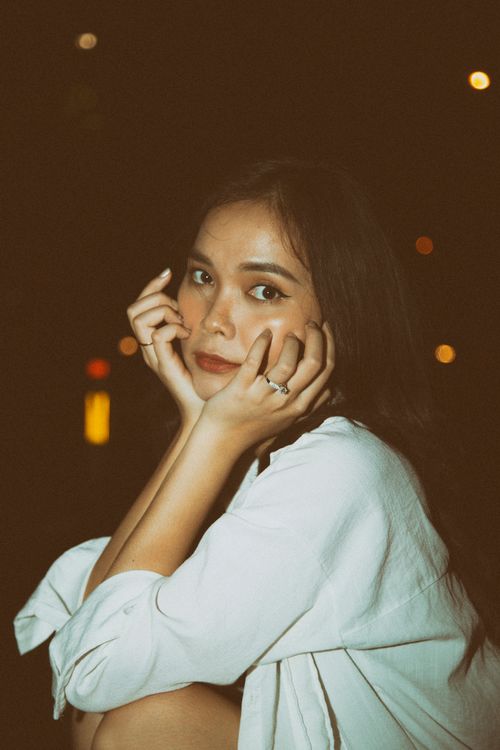 Free A young woman in a white shirt posing thoughtfully under city lights at night. Stock Photo