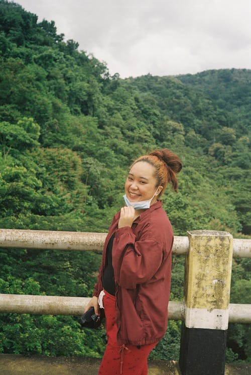 Woman in a Maroon Jacket Wearing Face Mask Posing near the Railings