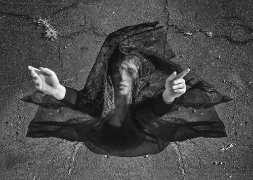 Free Black and white image of a woman in black cloth reaching up from cracked asphalt. Stock Photo