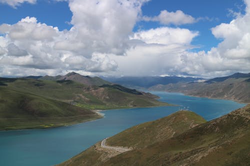 Green Mountains Near Body of Water Under White Clouds and Blue Sky