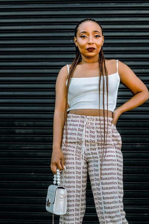 Free Fashionable woman posing with braided hair and printed pants against a dark background. Stock Photo