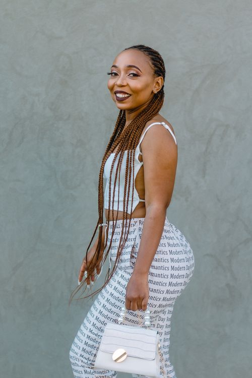 Free Happy woman with braided hair in a fashionable outfit carrying a stylish white handbag. Stock Photo