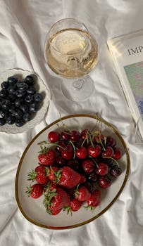 A top view of fresh strawberries, cherries, and blueberries paired with white wine in an elegant setting.