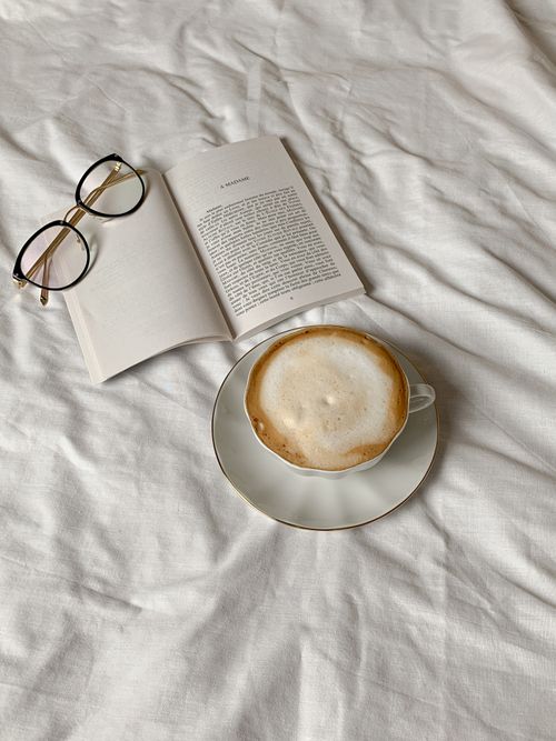 Free Relaxing scene with coffee cup, open book, and reading glasses on white fabric. Stock Photo