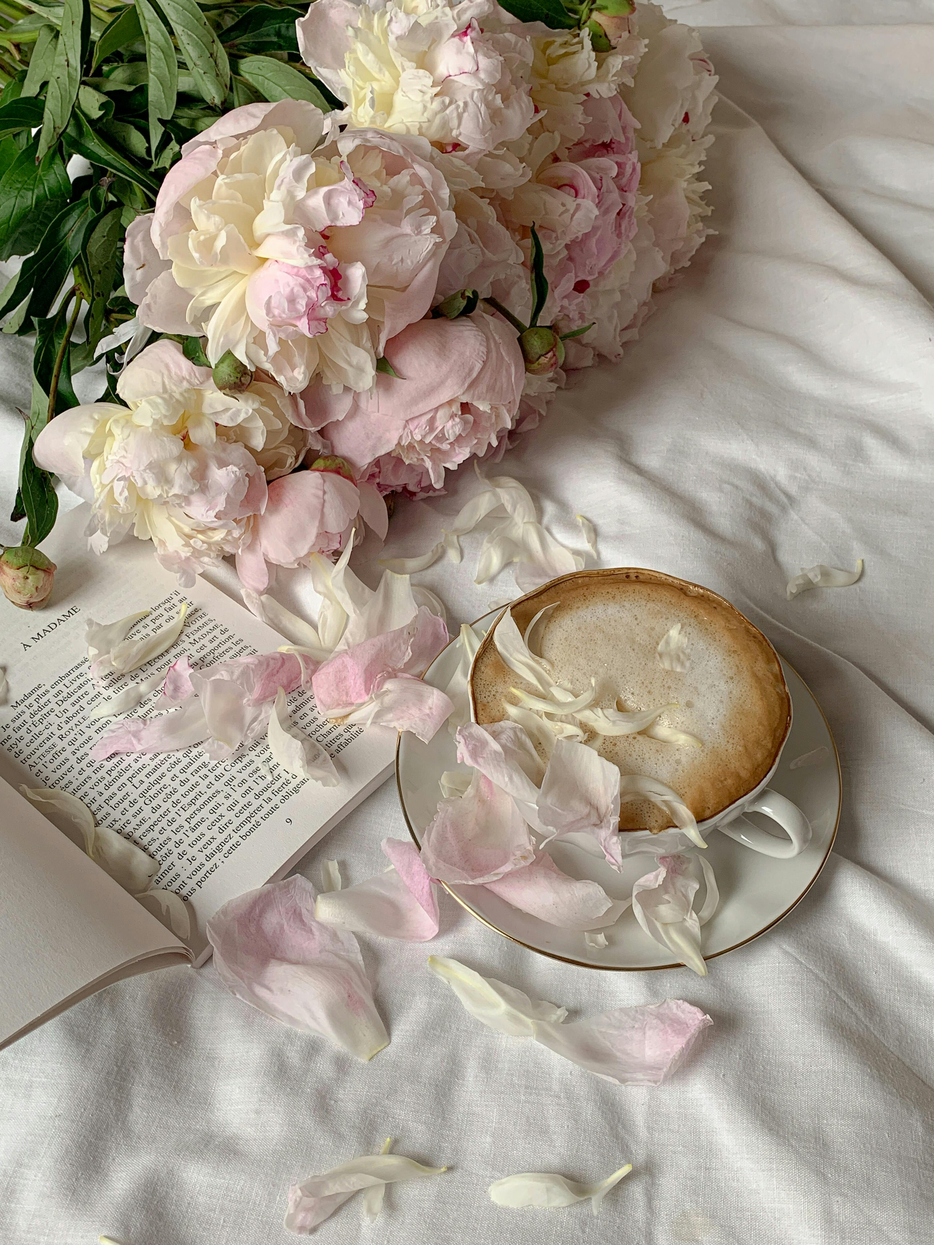 Free Stylish composition of peonies, a coffee cup, and an open book on soft linens, evoking a serene morning mood. Stock Photo