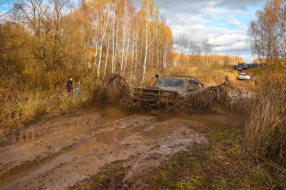 4x4 vehicle splashes through muddy forest path during off-road adventure.