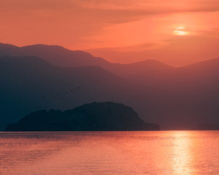 Enchanting sunset with mountains, birds, and ocean, perfect for serene landscapes.