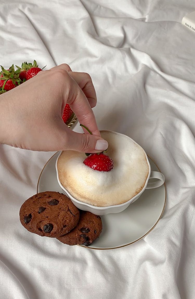 A Person Holding Strawberry Dipping In The Coffee 