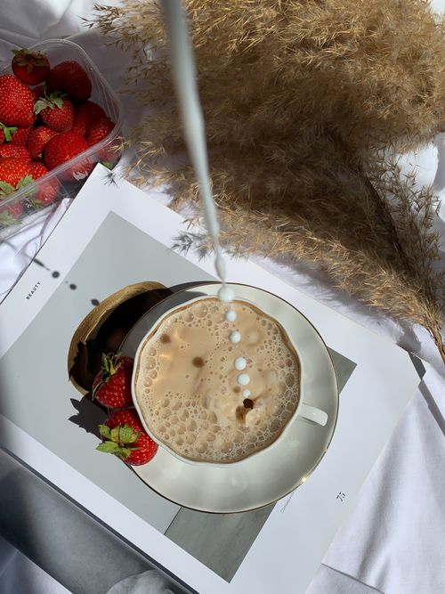 Free Aesthetic high-angle shot of milk pouring into coffee with fresh strawberries and decorative dried leaves. Stock Photo