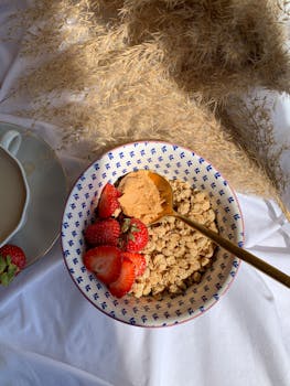 A top view of a breakfast bowl with granola, strawberries, and peanut butter on a white cloth.