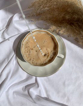 Aesthetic overhead shot of milk being poured into a coffee cup on a saucer.
