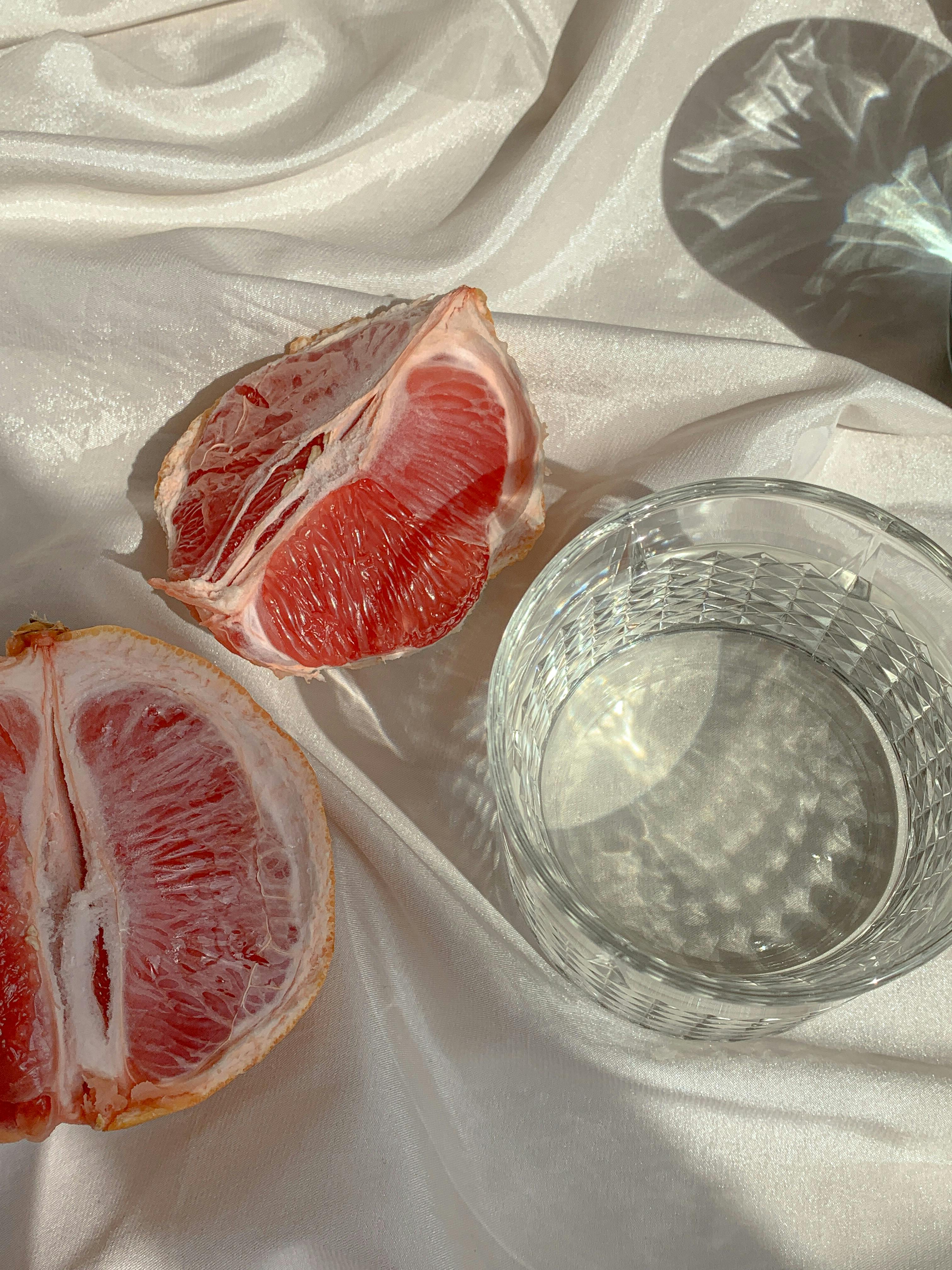 Close-up of sliced grapefruit and glass of water on a satin surface, capturing light reflections.