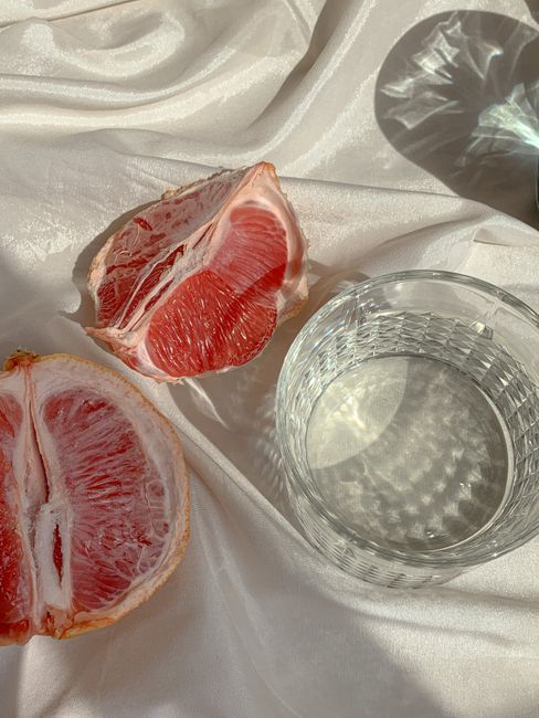 Close-up of sliced grapefruit and glass of water on a satin surface, capturing light reflections.