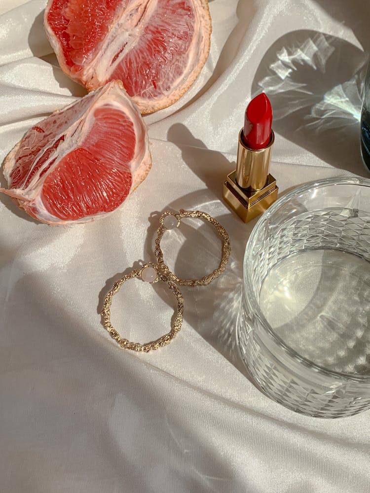 Red Lipstick And Hoop Earrings Beside A Clear Glass Cup