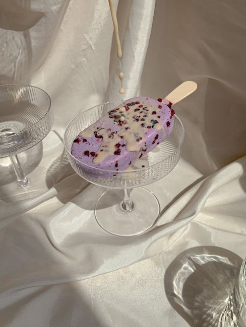 Lavender-colored ice cream popsicle with sprinkles on glass cup, melt dripping.
