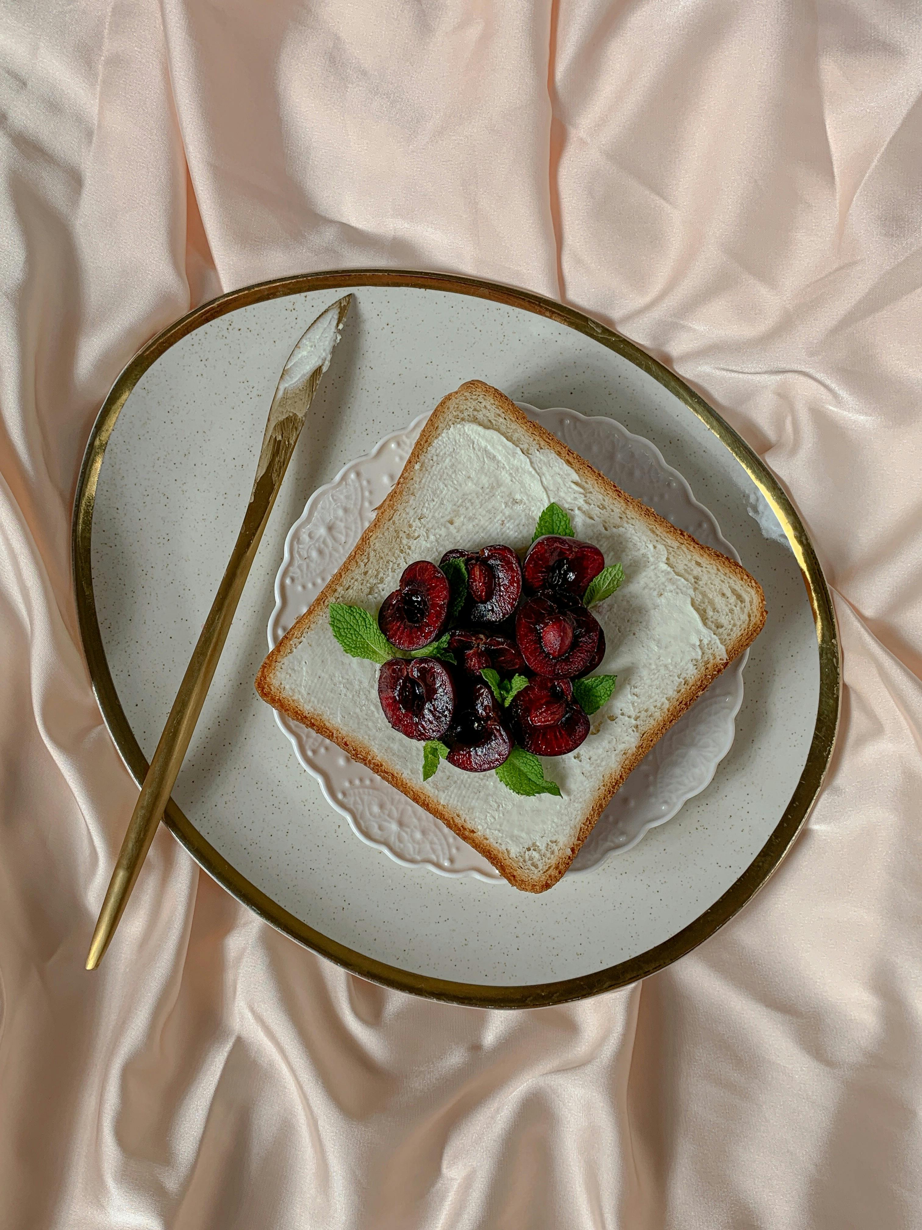 bread and cherries on a white and gold plate