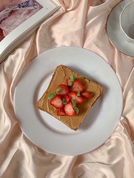 Peanut butter toast topped with strawberries on satin fabric, perfect breakfast setting.