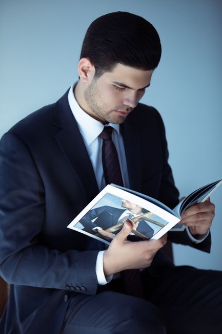 Young business professional in a suit reading a magazine indoors, focused and intellectual. Young business professional in a suit reading a magazine indoors, focused and intellectual.