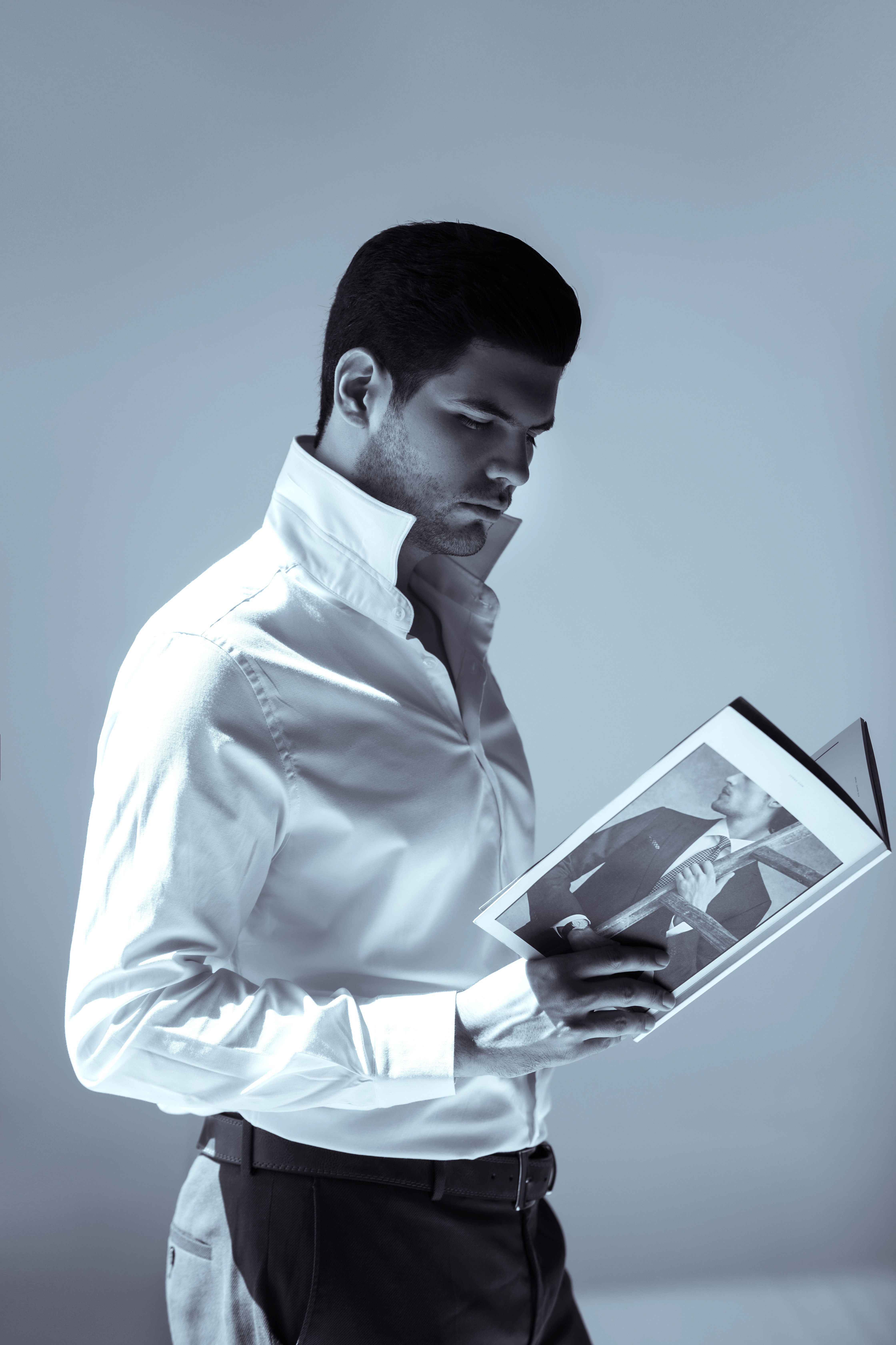 A stylish man in a white shirt reads a fashion magazine in monochrome lighting.
