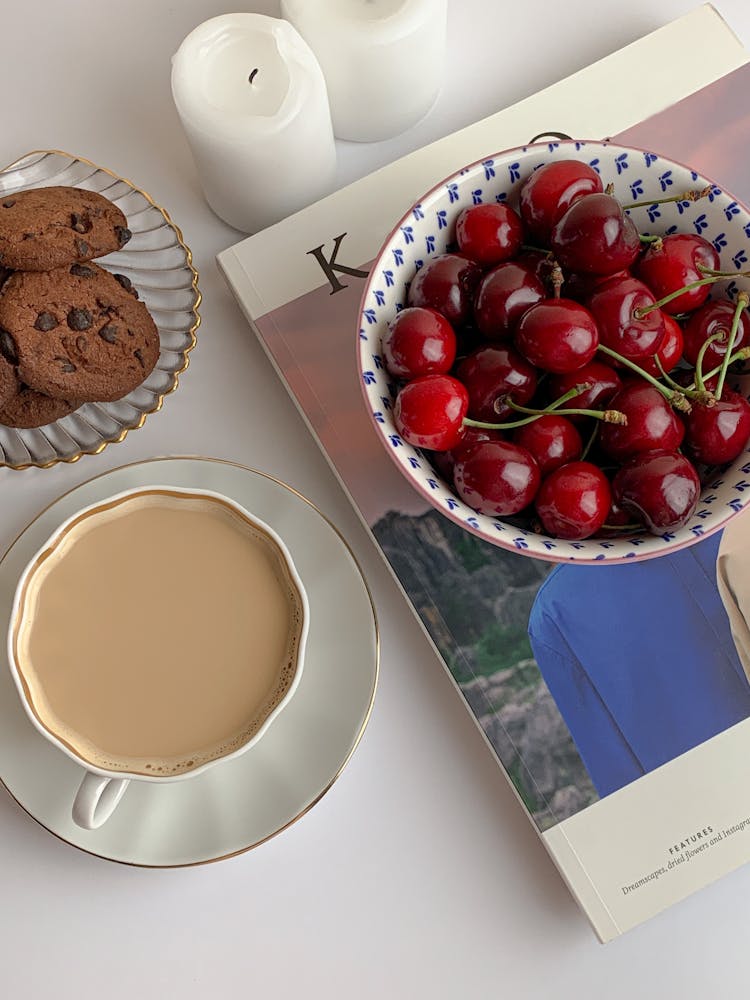 A Cup Of Coffee Beside A Bowl With Cherries