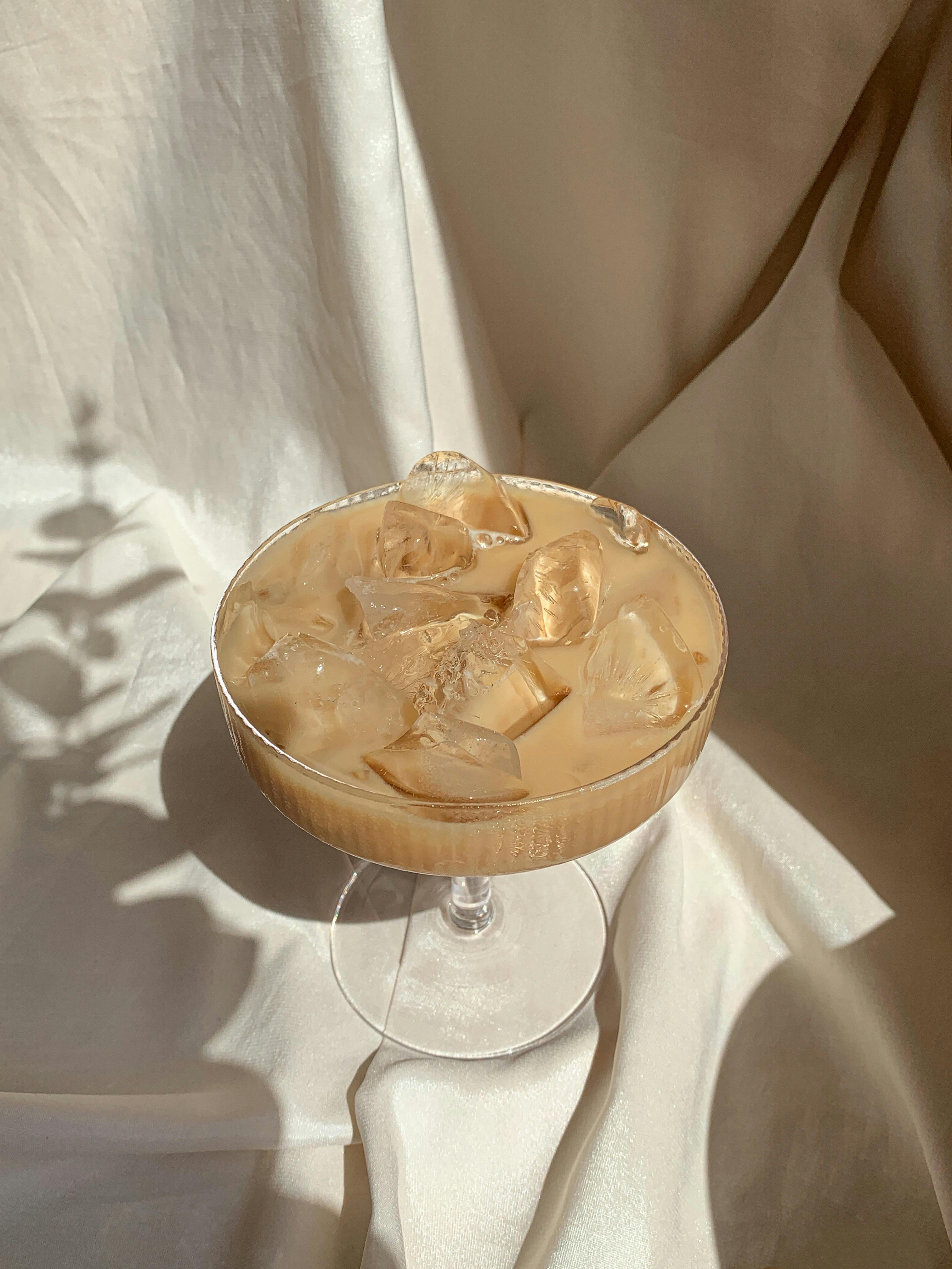Elegant still life of iced coffee with ice cubes in a glass against a silky fabric backdrop.