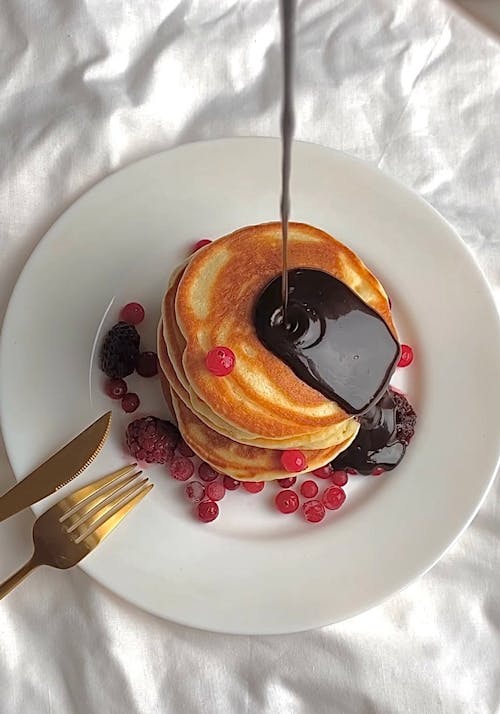 Free Close-Up Shot of Stack of Pancakes with Chocolate Syrup on a White Plate Stock Photo