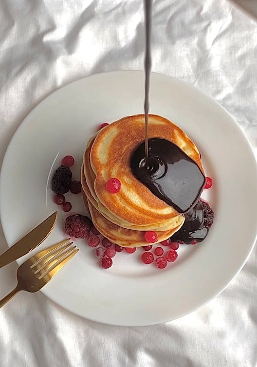 Close-Up Shot of Stack of Pancakes with Chocolate Syrup on a White Plate