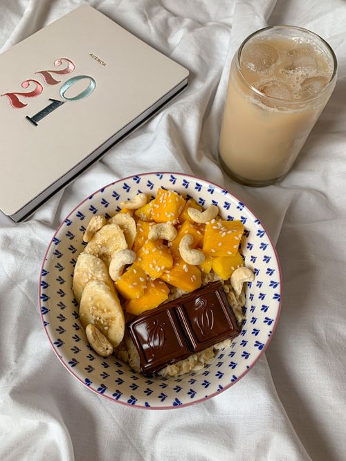 Free Delicious breakfast bowl with fruits, nuts, and chocolate, alongside iced coffee on white fabric. Stock Photo