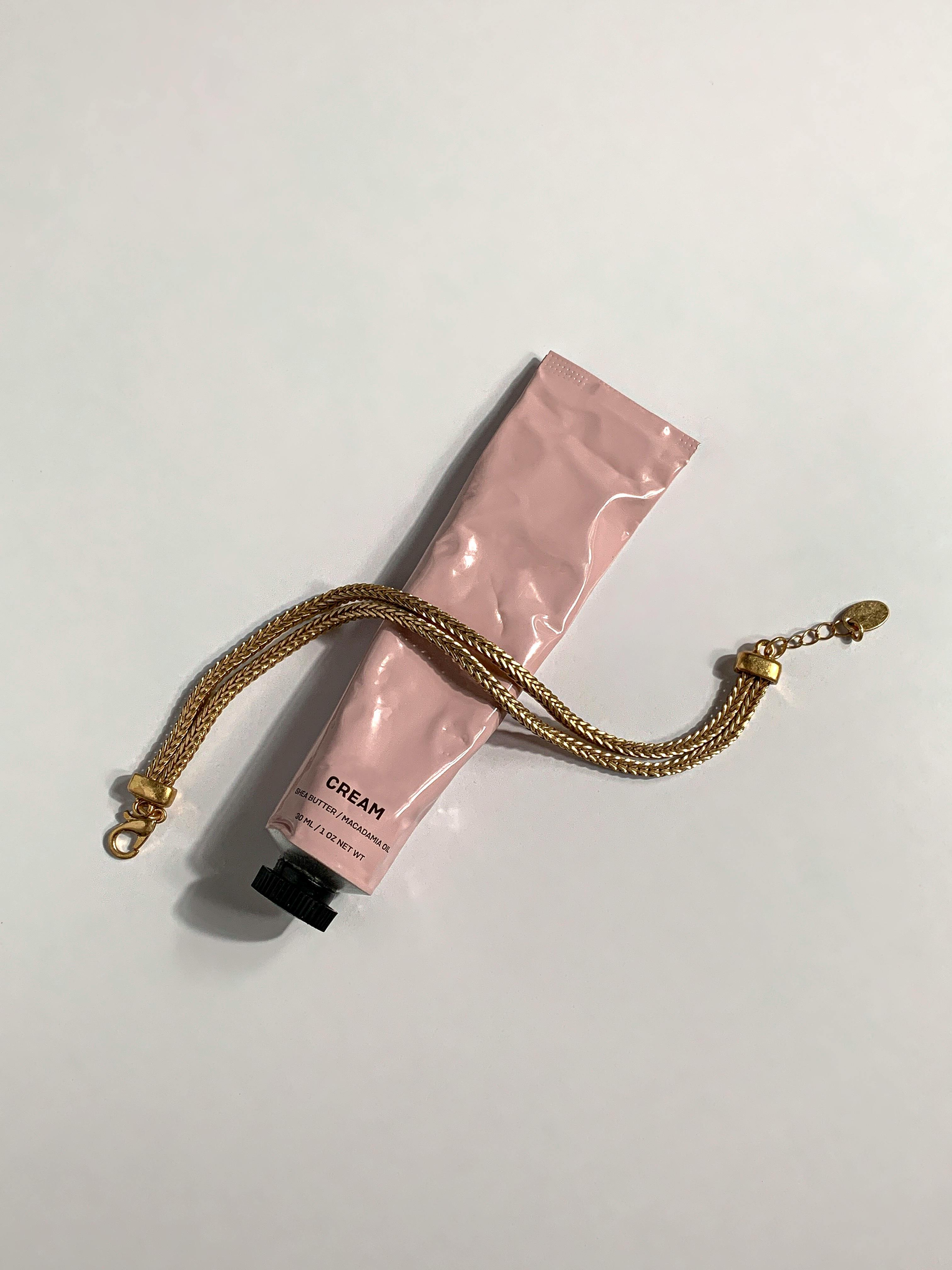 gold bracelet a pink tube container on a white surface