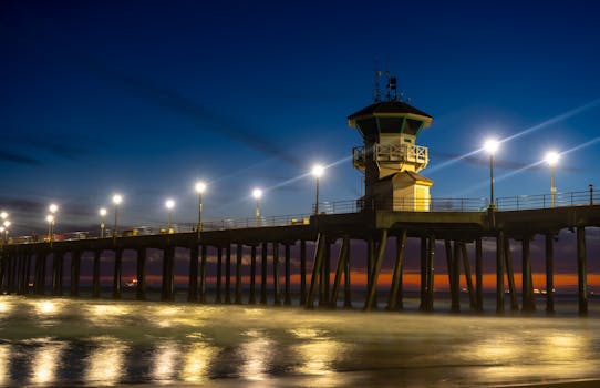 Scenic view of Huntington Beach Pier at dusk, illuminated by lights over the Pacific Ocean.
