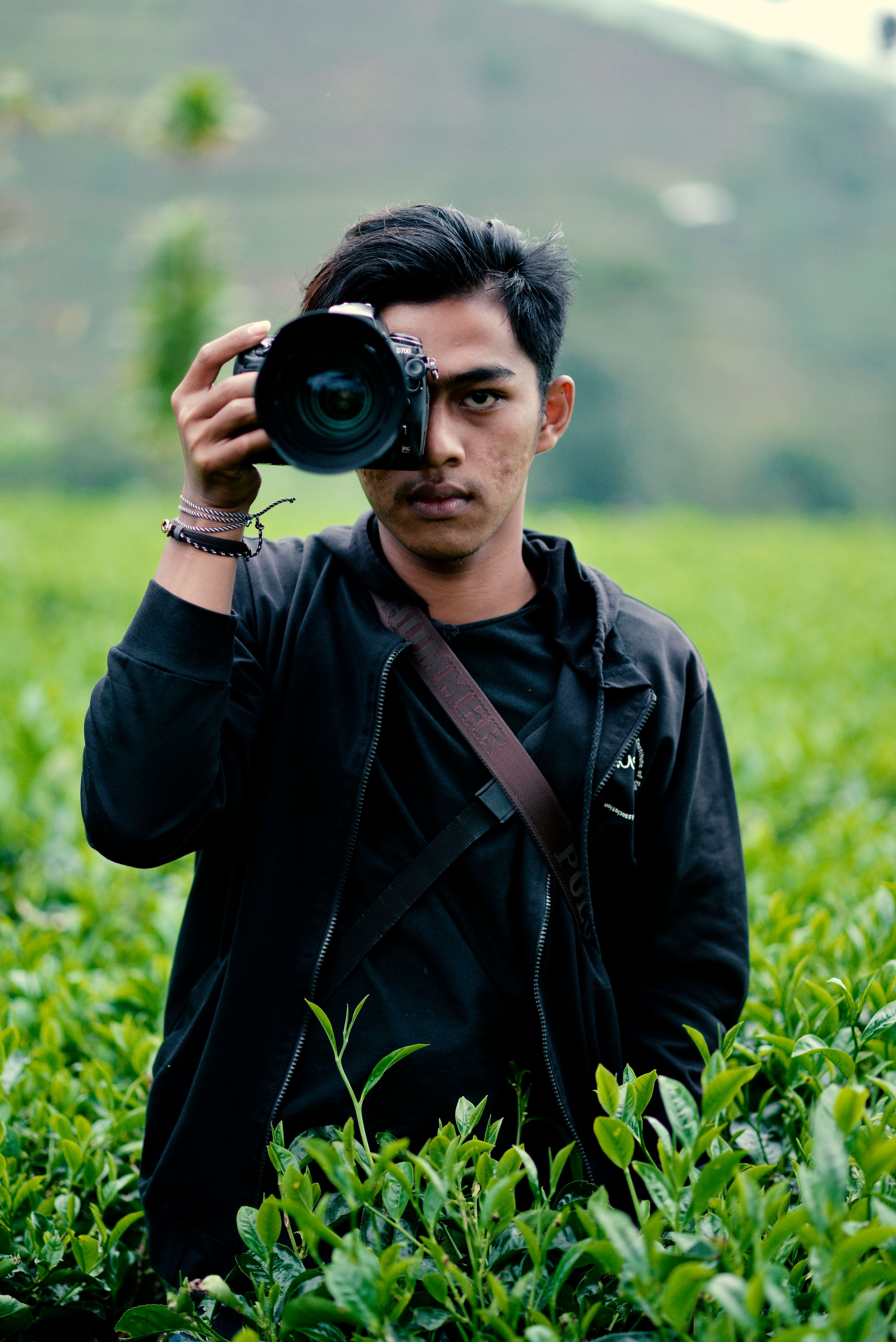A young man takes photos in a lush green field with his DSLR camera.