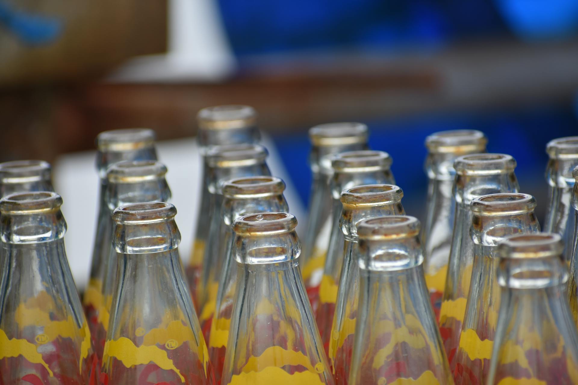 Empty glass soda bottles arranged in rows with colorful labels, perfect for recycling themes.