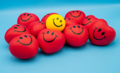 Free Heart-shaped red and yellow smiley stress balls on a blue surface conveying positivity and stress relief. Stock Photo