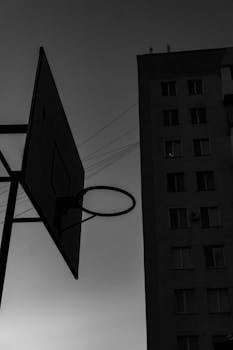 A monochrome image of a basketball hoop silhouette with a building and power lines.