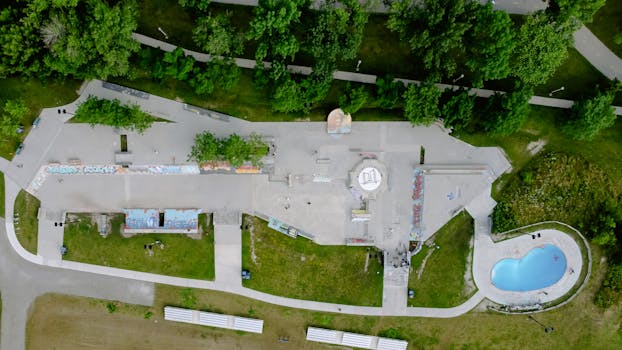 A top-down drone shot of an urban skatepark and pool nestled amidst lush green trees.