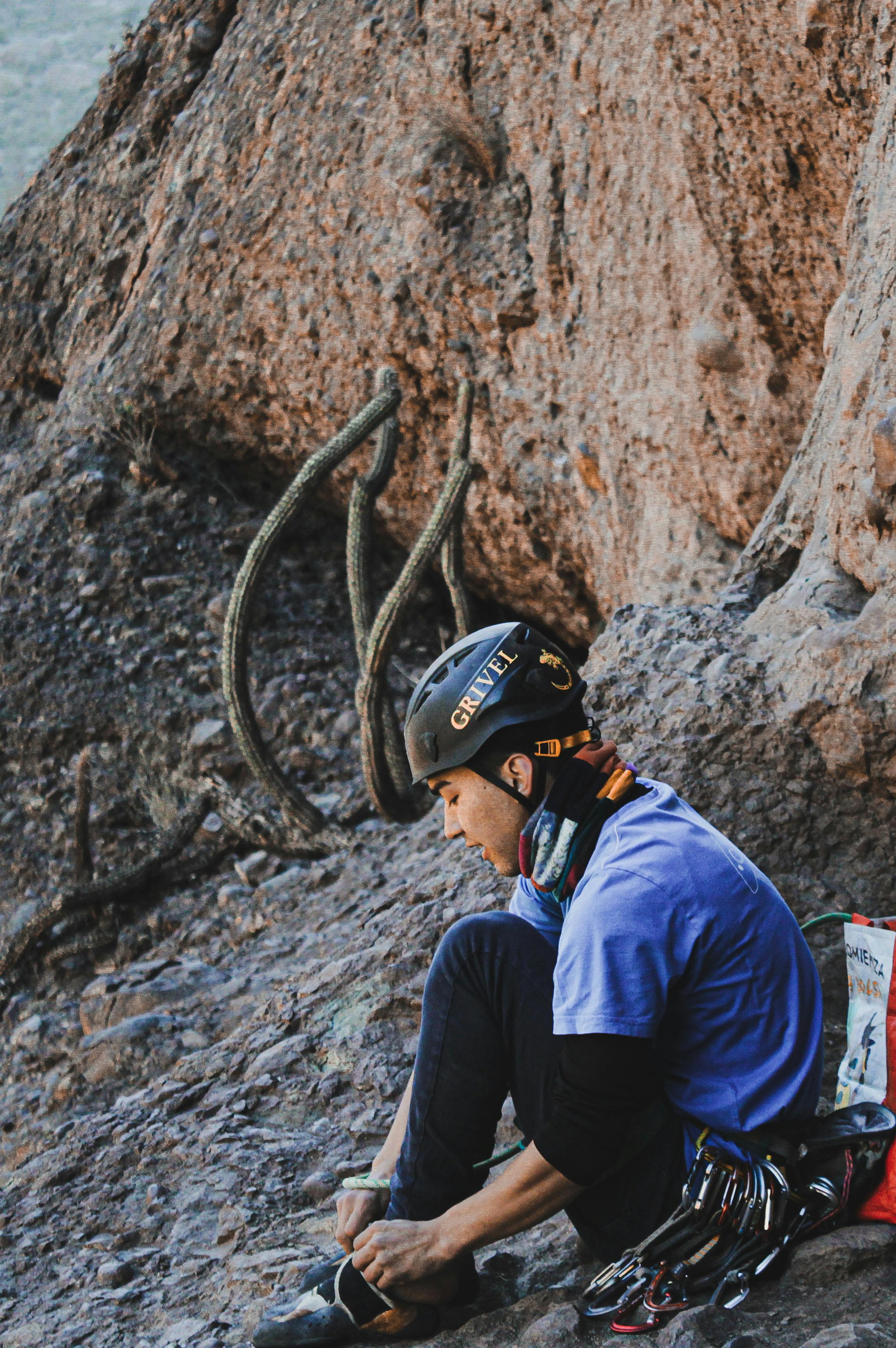 Woman rock climber adjusts gear before scaling rocky terrain. Outdoor adventure scene.