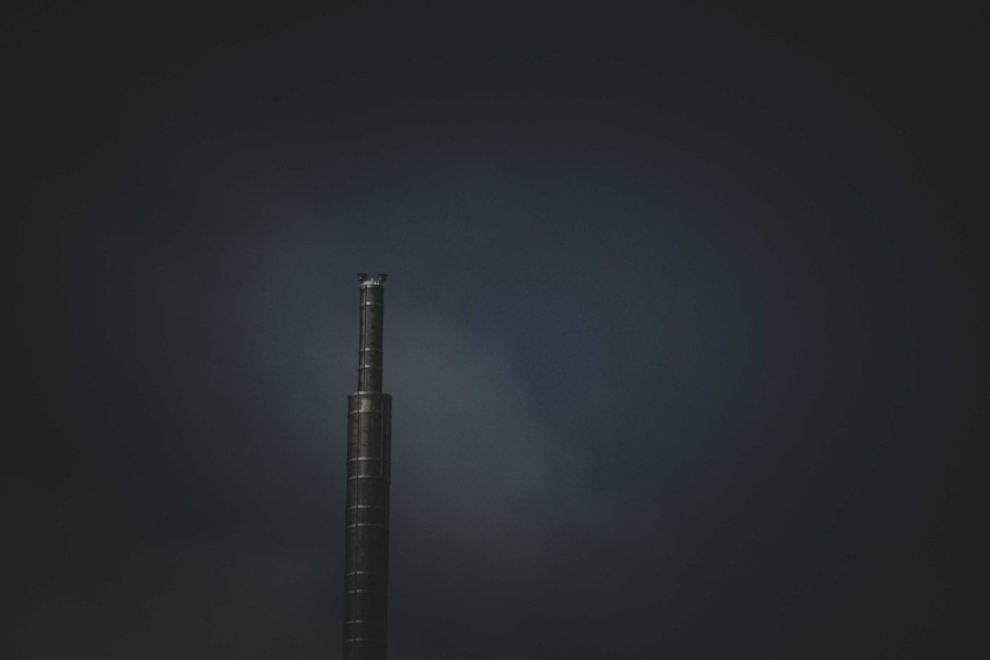 A lone industrial chimney emitting smoke against a dark sky, symbolizing air pollution.