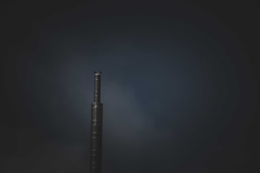 A lone industrial chimney emitting smoke against a dark sky, symbolizing air pollution.