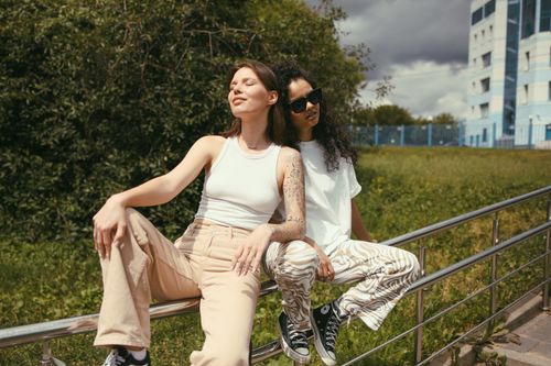 Free Two women sitting on railings, enjoying a sunny outdoor day with a relaxed and happy vibe. Stock Photo