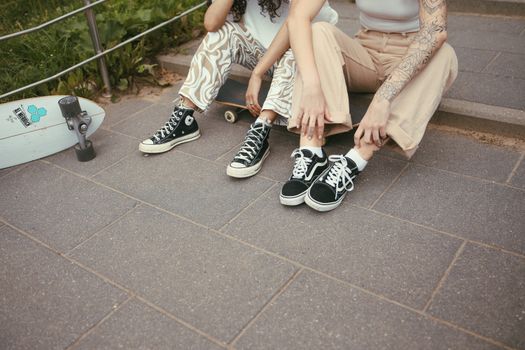 Two women sitting with skateboards on city steps, showcasing a relaxed, urban lifestyle.