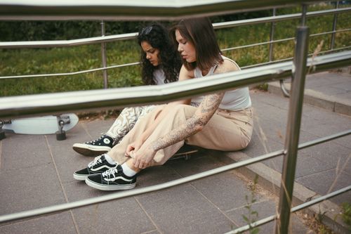 Free Two young women sitting on steps with skateboards, enjoying a summer day outdoors. Stock Photo