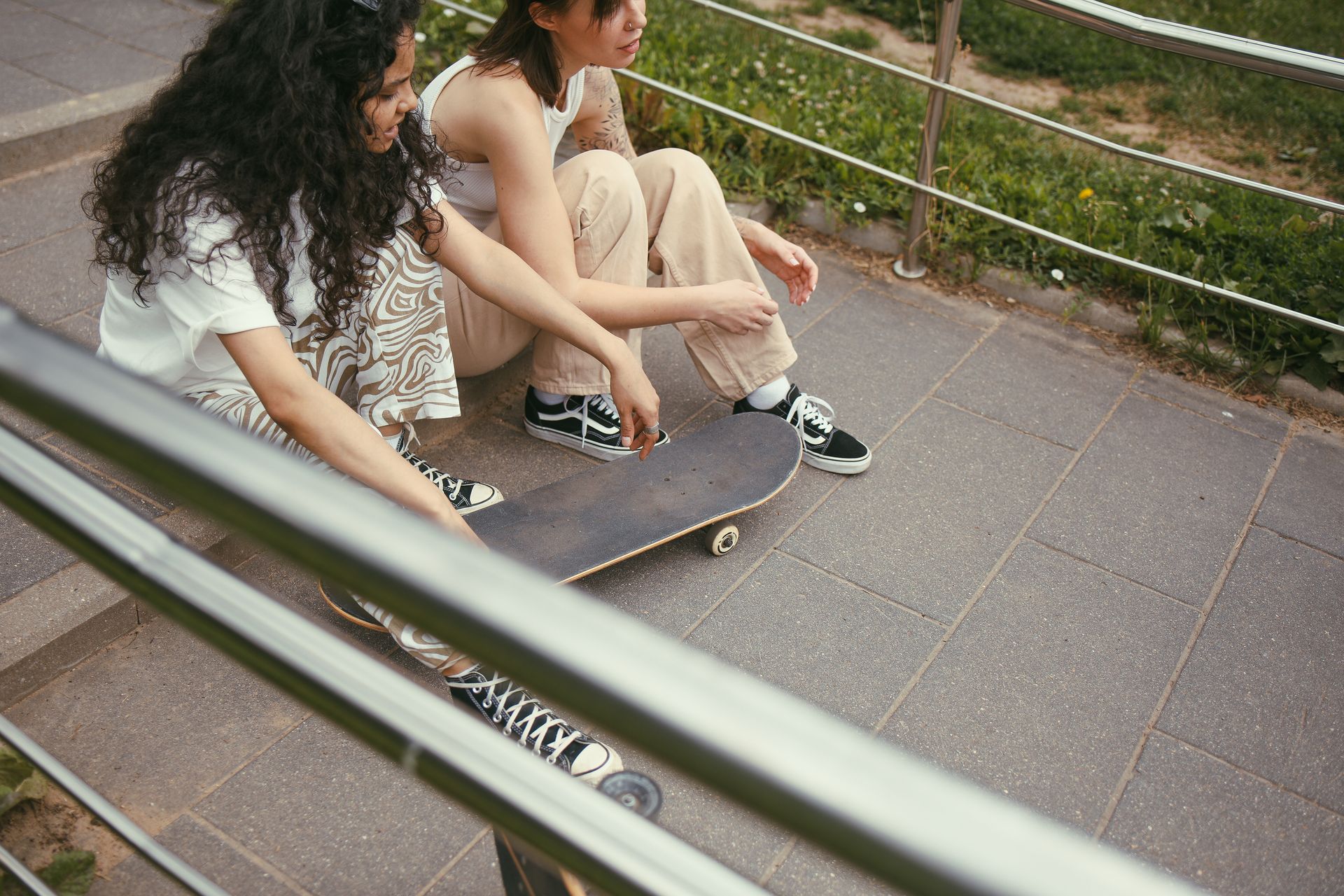 Two female skaters sitting on steps with a skateboard outdoors.
