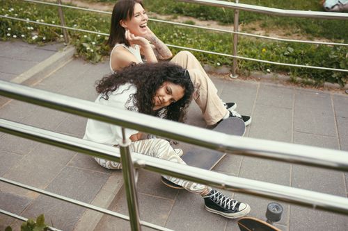 Free Two young women sitting on skateboards, smiling and enjoying a sunny day outdoors. Stock Photo