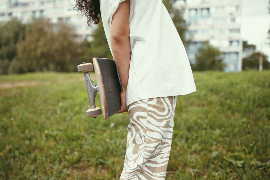A person standing outdoors holding a skateboard with a grassy park background.
