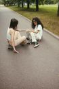 Woman in White Shirt and White Shorts Sitting on Gray Asphalt Road