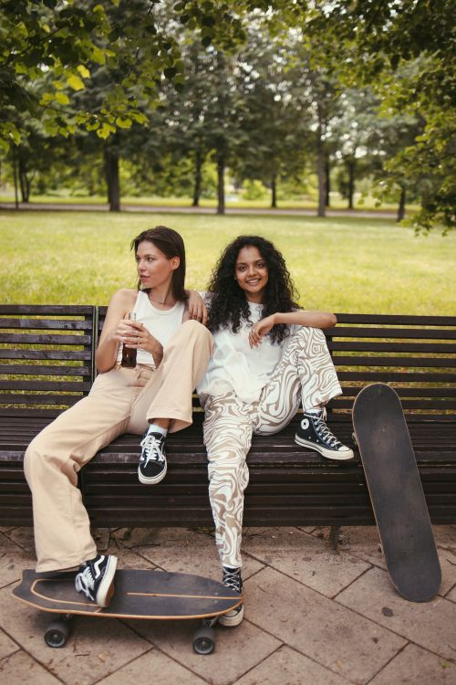 Free Two young women on a bench with skateboards enjoying a sunny day in the park. Stock Photo